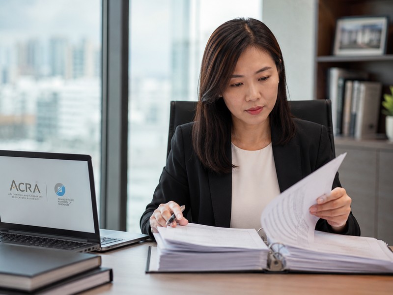 How to Rectify Past Non‑Compliance and Clean Up Your Company Records A professional photo of a corporate secretary at a desk reviewing company registers and documents, with ACRA and IRAS lo