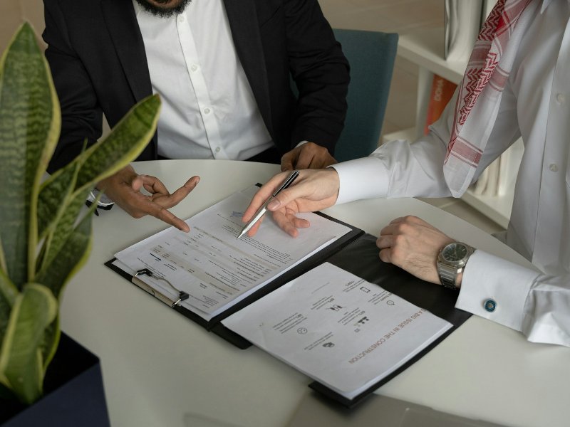 Two men at a table with papers and a pen, representing shareholders reviewing an agreement