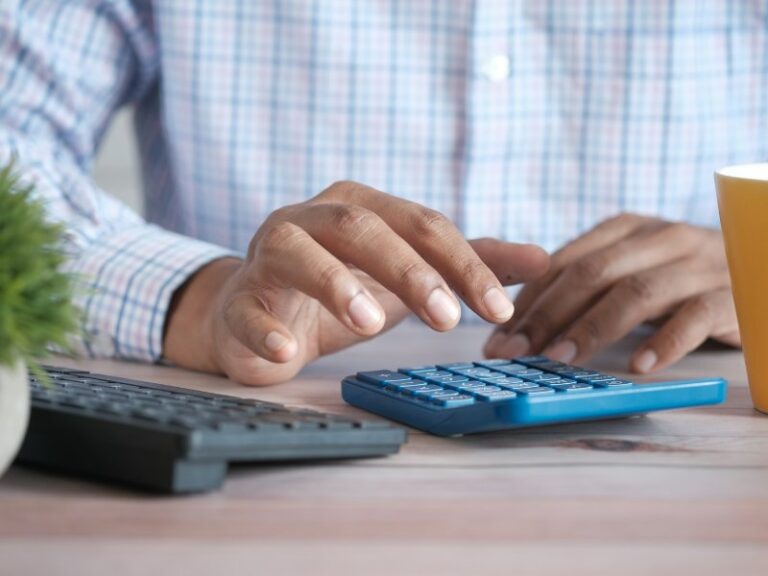 Person using a calculator at a desk beside a coffee mug