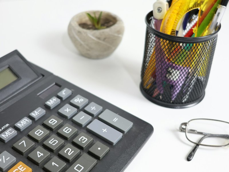 Calculator, glasses and pens on a white desk, representing year-end bonus and directors' fee calculations