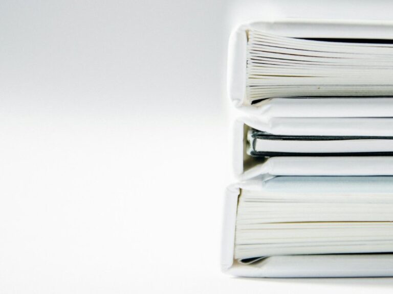 A tall stack of thick paper folders on a white surface