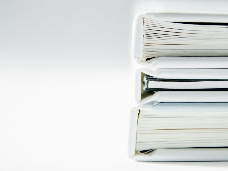 A tall stack of thick paper folders on a white surface