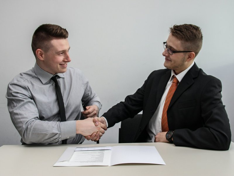 Two businessmen shaking hands across a table with a signed contract in front of them