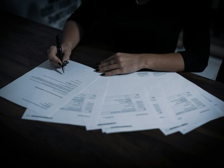 Business owner reviewing and signing a spread of documents at a dark wooden table
