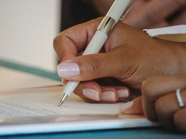 Close-up of a hand signing a document with a white pen, representing a tender submission