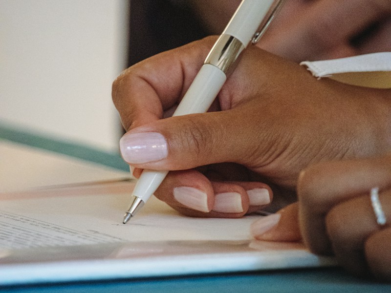 Close-up of a hand signing a document with a white pen, representing a tender submission