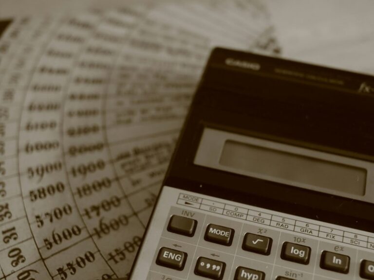 Calculator resting on printed financial ledger sheets with columns of figures
