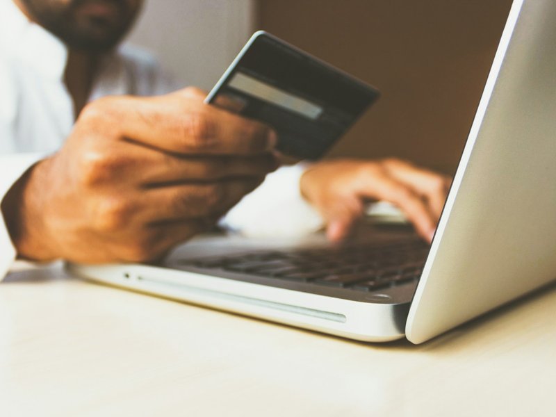 Person holding a payment card while using a laptop to make an online purchase