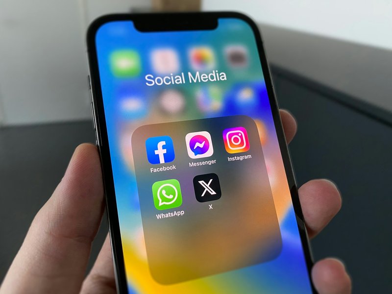 Hand holding a smartphone showing a folder of social media apps