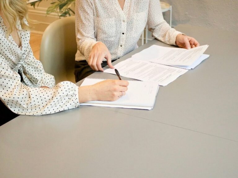 Woman signing a printed document while another person points to the papers