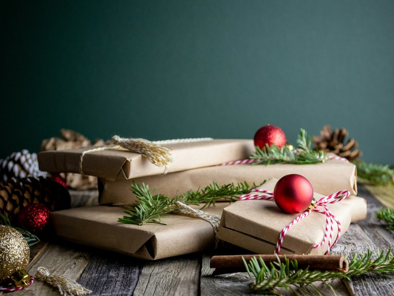 Brown paper-wrapped gift boxes tied with string and red baubles on a wooden table