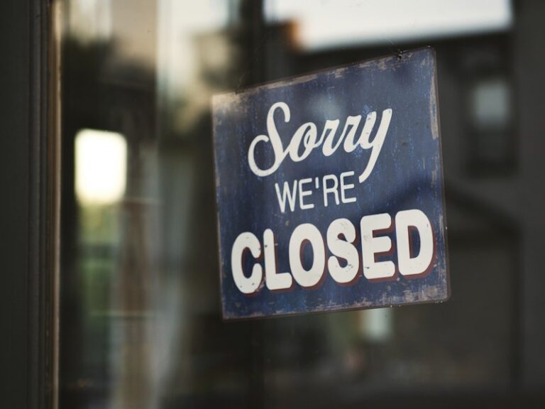 A 'Sorry, we're closed' sign hanging on a glass shop door