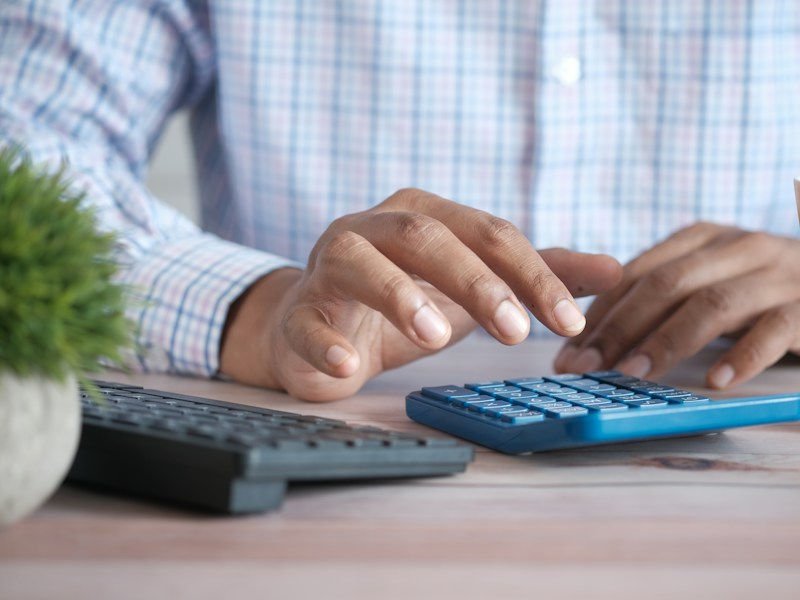Close-up of a hand using a calculator at a desk, illustrating CPF bonus calculations for December payroll