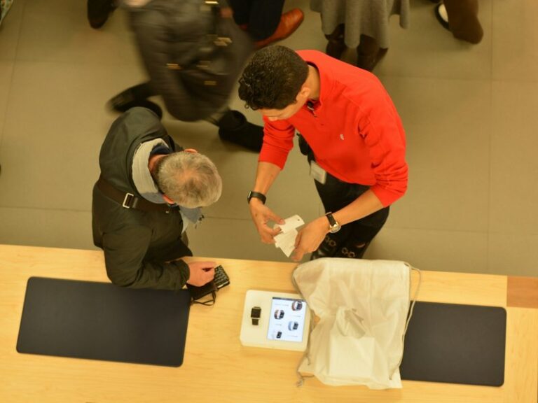 A store employee helps a customer at a retail counter, seen from above