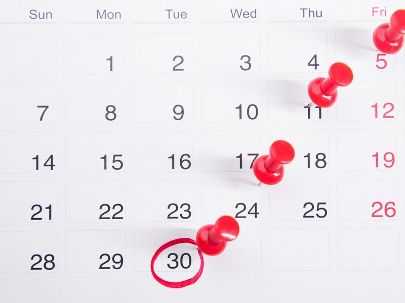 Wall calendar with red push pins marking dates and the 30th circled in red, representing the deadline to sue for an unpaid debt