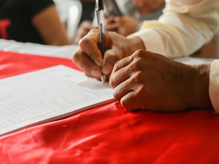 A man signing a printed form with a pen at a table with a red cloth