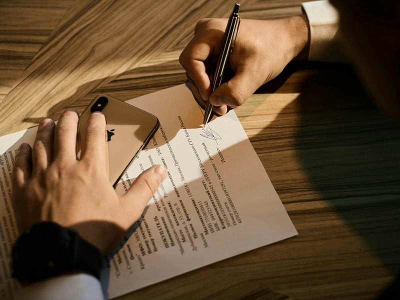 Person signing a loan document at a wooden desk