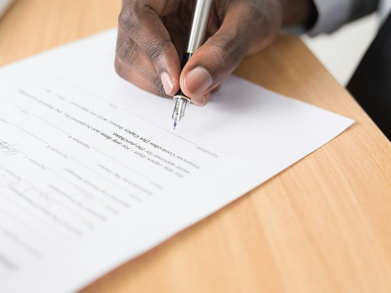 Hand holding a fountain pen signing a printed contract on a wooden desk