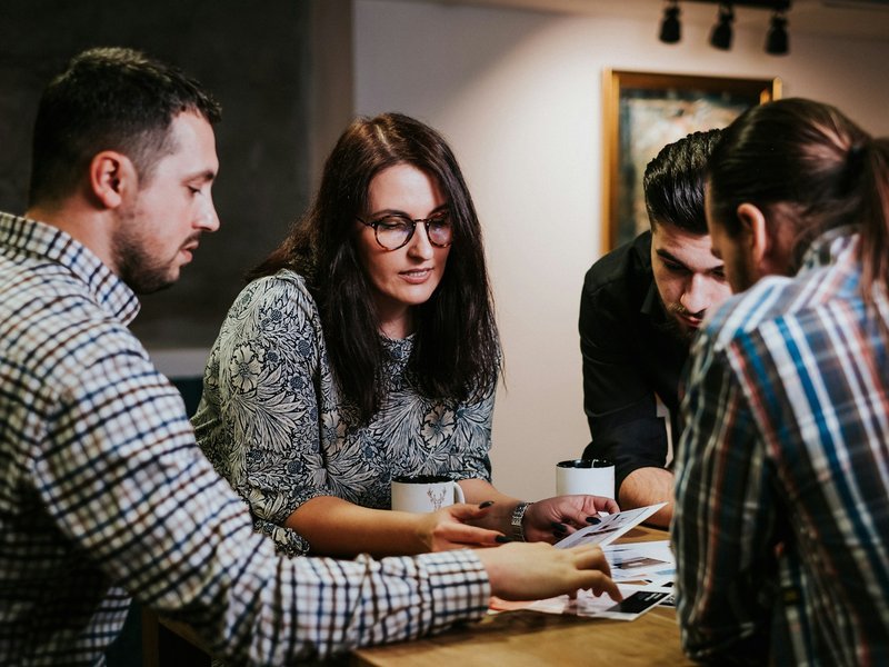 Four colleagues reviewing documents together at a wooden table in an office