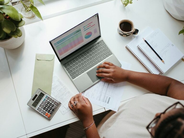 Person reviewing printed invoices beside a laptop and calculator on a desk
