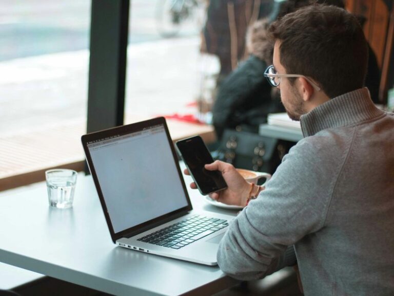 Man working on a laptop and smartphone at a cafe table by a window