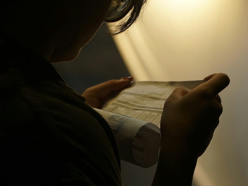 Person in a dimly lit room closely examining a folded printed document