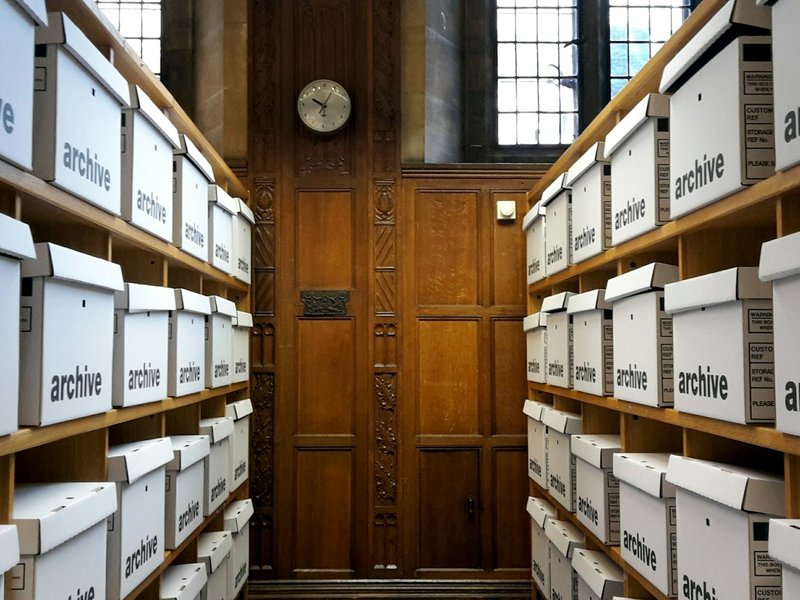 Rows of white archive boxes on wooden shelves in a records room
