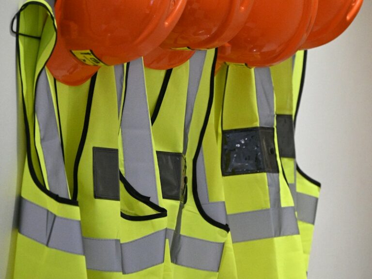 Row of high-visibility safety vests and orange hard hats hanging unused on a wall