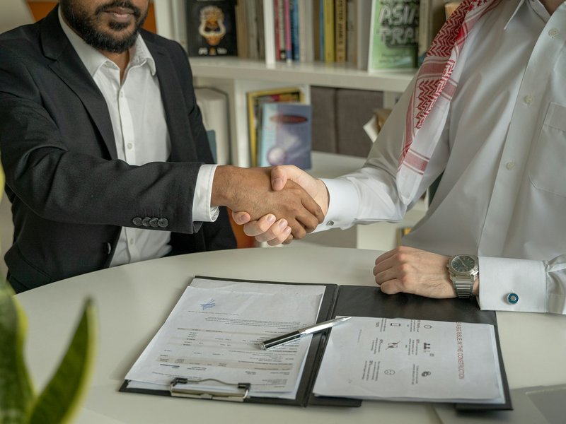 Two businessmen shaking hands across a table with settlement documents and a pen