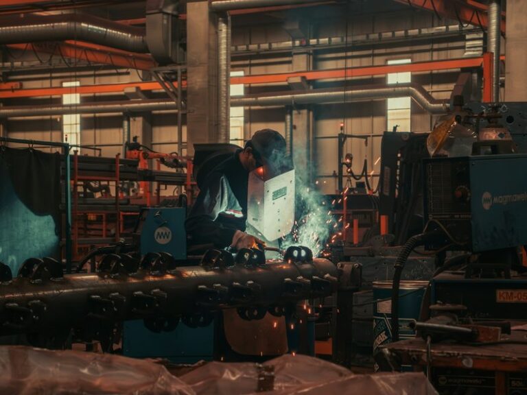 Welder in a protective mask working on a steel pipe in a factory workshop
