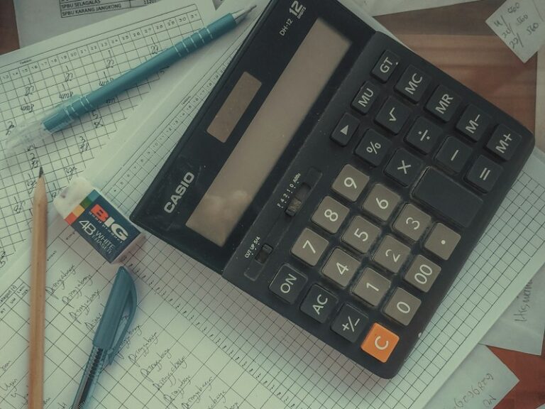 A desk calculator on handwritten payroll and attendance sheets with pens and a pencil
