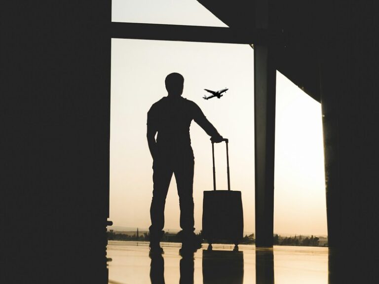 Silhouette of a business traveller with a suitcase watching a plane take off from an airport terminal window