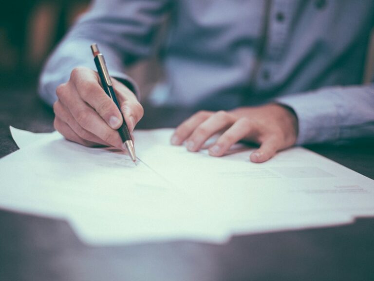Man in a light blue shirt signing a document with a pen at a desk