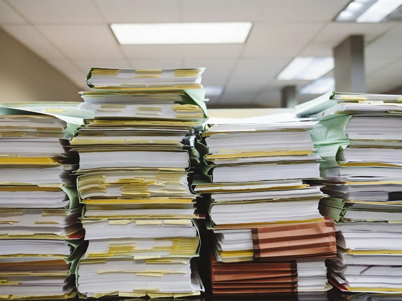 Tall stacks of paper files and folders with yellow tabs in an office