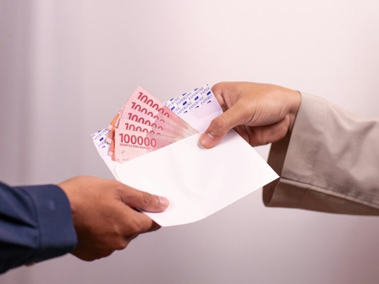 Cash in a white envelope being handed from one person to another