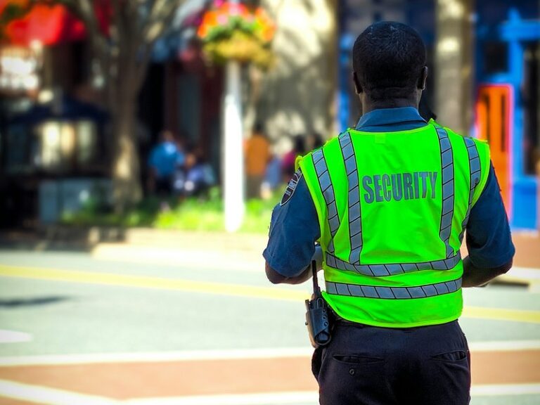 Security officer in a high-visibility vest marked SECURITY, seen from behind at a street crossing