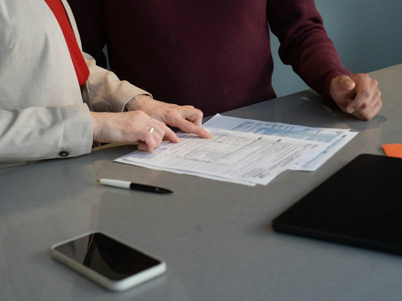 Two people reviewing printed documents at a table with a pen and phone nearby