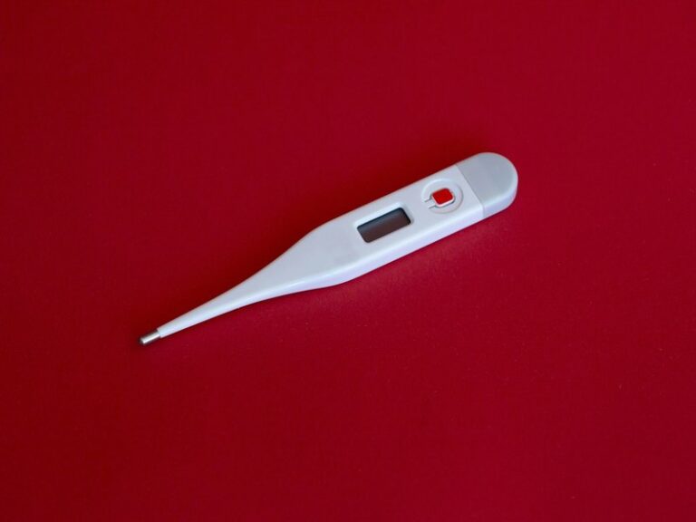 White digital thermometer lying on a red surface