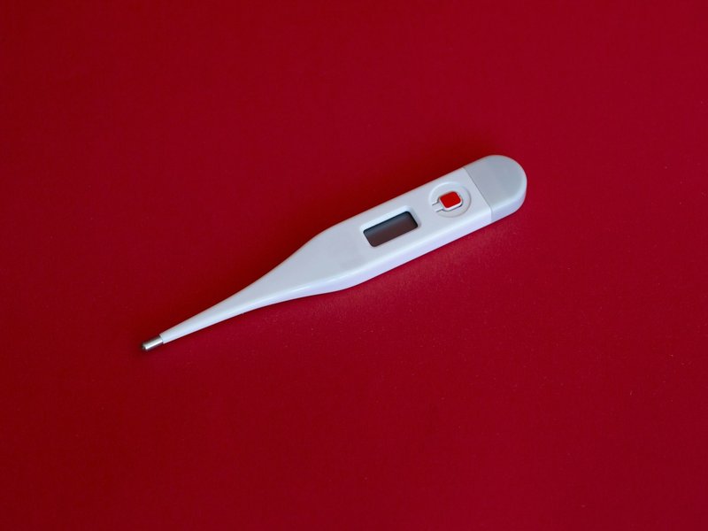 White digital thermometer lying on a red surface