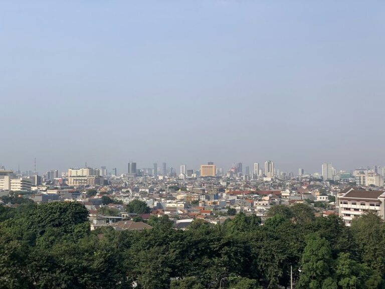 Jakarta skyline of high-rise towers seen above green trees under a clear sky