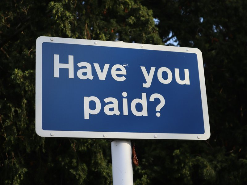 Blue road sign reading 'Have you paid?' against dark green trees