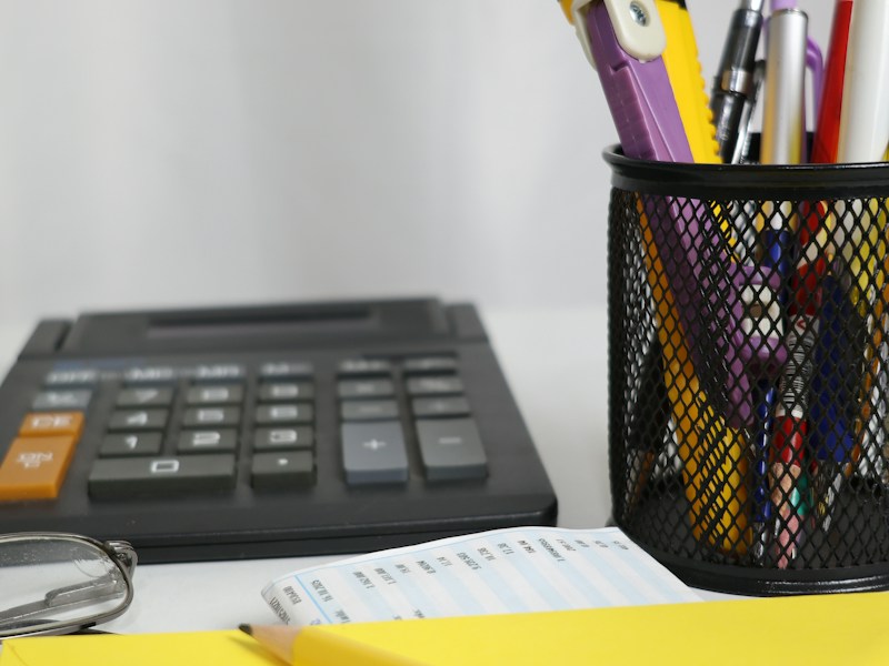 Office desk with a calculator, pens, a printed receipt and a yellow envelope, representing invoices and paperwork for a small claim