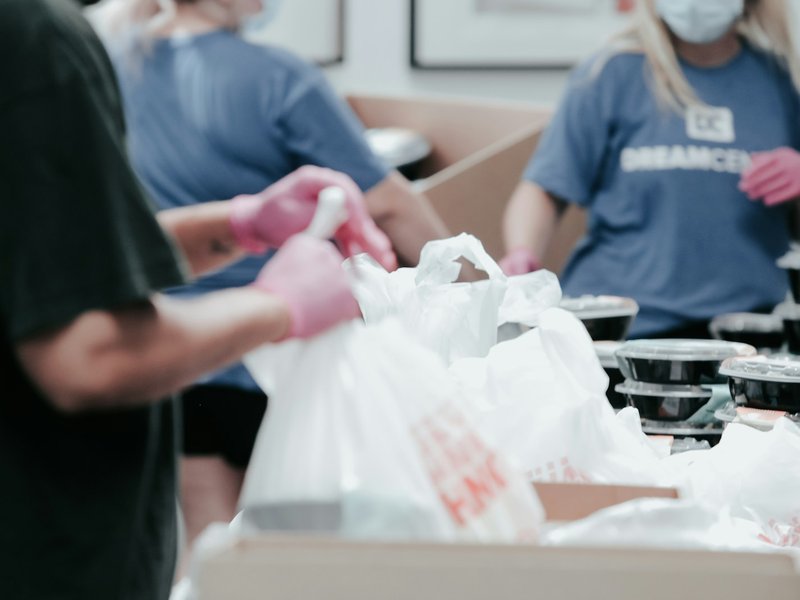 Volunteers in blue shirts and pink gloves packing food into white plastic bags