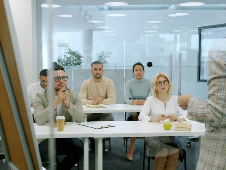 Employees seated at a table listening to a trainer during an office training session