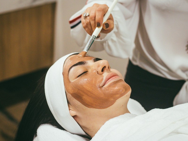 Beautician applying a facial mask with a brush to a client at a spa