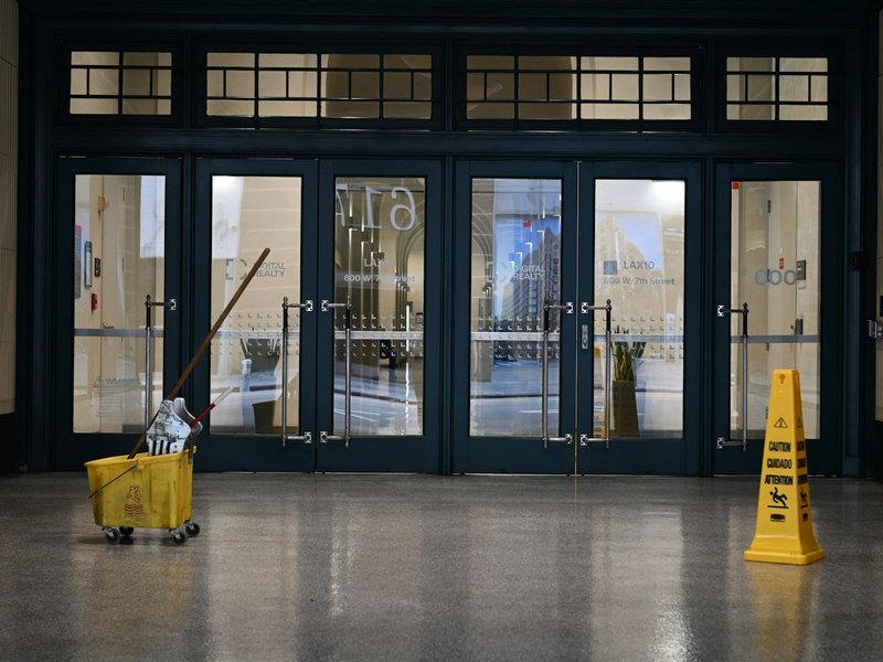 A yellow mop bucket and a wet floor caution sign on a polished lobby floor in front of glass entrance doors