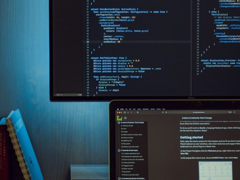 A computer monitor and laptop displaying programming code on a developer's desk