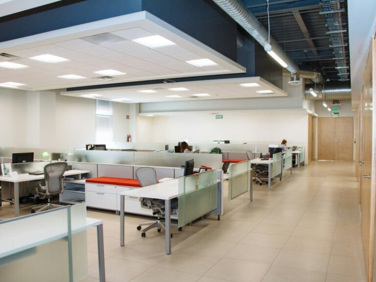 Open-plan office with rows of white desks and frosted glass partitions