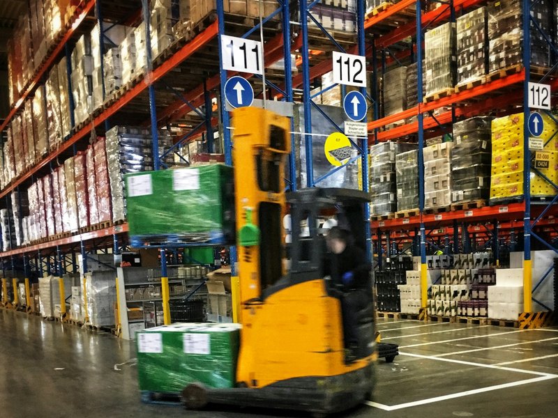 Forklift moving wrapped pallets of stock along racking in a warehouse