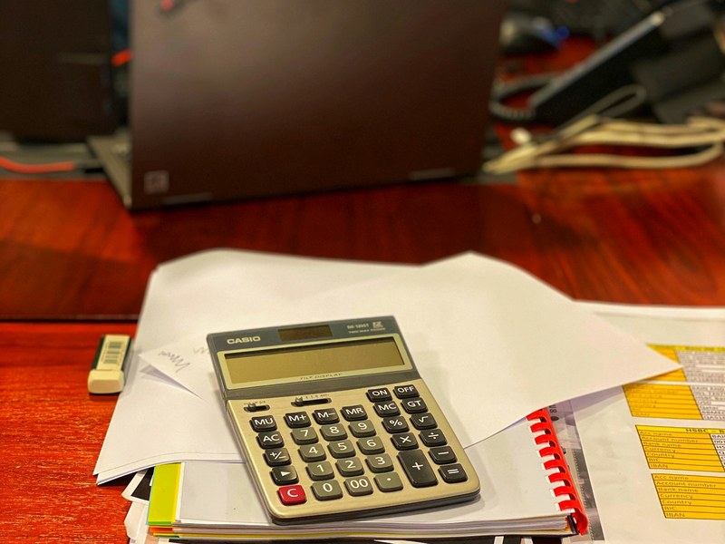 Calculator resting on a stack of papers and payroll documents on an office desk